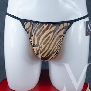 May include: A sheer thong with a zebra print in tan and black. The underwear has a black trim and thin straps. The garment is displayed on a white mannequin.