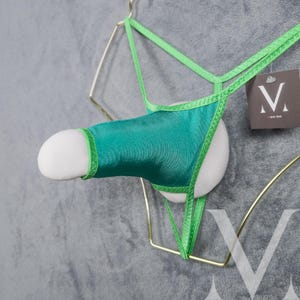 Peut inclure: Sous-vêtements en résille vert avec un rembourrage en mousse blanche. Les sous-vêtements sont présentés sur un cintre doré.