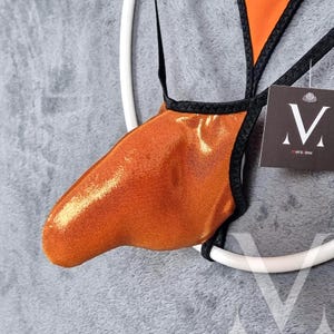May include: Orange and black swimwear with a metallic sheen. The swimsuit has a unique design with a V-shaped top and a thong bottom. A small tag with a stylized "V" logo is attached.