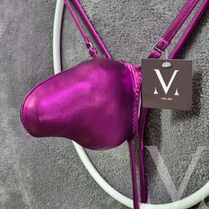 May include: A purple satin jockstrap with a shiny finish. The strap has a small tag with the letter "M" and the text "mens lev" on it.