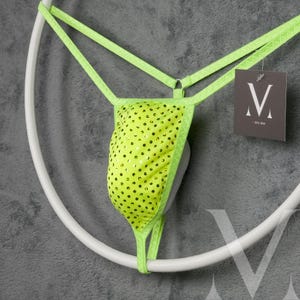 May include: A neon green thong with a polka dot pattern, displayed on a white circular hanger. The thong has a matching trim and straps. A tag with the letter "V" is attached.
