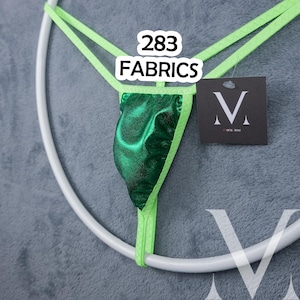 May include: A green thong with a metallic sheen, accented with neon green straps. The text "283 FABRICS" is displayed above the garment. A tag with the "V" logo is attached.