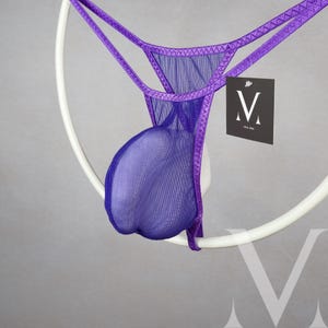 Könnte beinhalten: Lilafarbener Netz-String mit lilafarbenem Besatz. Der String hängt an einem weißen Ring.