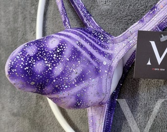 May include: Purple and silver glitter swimsuit with a tie-back design. The swimsuit has a swirl pattern and is made of a shiny fabric. The tag on the swimsuit reads "Mensview".