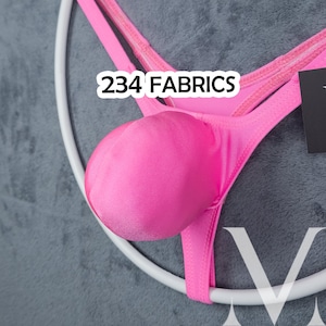 Può includere: Perizoma rosa acceso con parte anteriore arrotondata, esposto su una gruccia bianca su sfondo grigio. Il testo "234 FABRICS" è visibile sull'indumento.