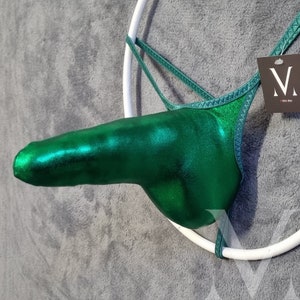 Puede incluir: Un tanga verde metálico con un diseño único. La prenda está suspendida por un aro blanco y tiene una etiqueta con un logotipo. La tela tiene una calidad brillante y reflectante.