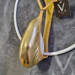 Könnte beinhalten: Goldfarbener Beutel mit einem gelben Band und einem weißen Futter. Das Band ist verstellbar und hat ein kleines Etikett mit dem Text "M" und "one size".