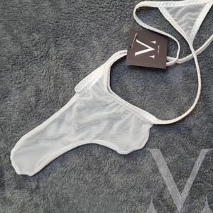 以下が含まれることがあります： 白いメッシュのランジェリーで、ストラップが1本と、小さな黒いタグに「V」の文字が書かれています。