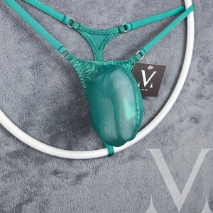 Könnte beinhalten: Ein grüner Netz-String mit V-förmigem Vorderteil und verstellbaren Trägern. Der String wird auf einem weißen Ring präsentiert.