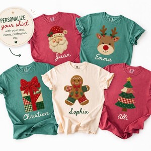 May include: Five short-sleeve t-shirts in red, green, and cream colors featuring Christmas graphics including Santa, a reindeer, a gift, a gingerbread person, and a tree. Each shirt displays a custom name in white cursive script text.