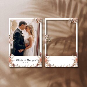 May include: Two white photo booth frames with floral accents. One frame contains a photo of a couple, the other is blank. The text "Olivia & Morgan" and the date "04.27.24" are printed at the bottom of the photo frame.