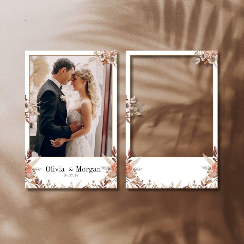 May include: Two white photo booth frames with floral accents. One frame contains a photo of a couple, the other is blank. The text "Olivia & Morgan" and the date "04.27.24" are printed at the bottom of the photo frame.