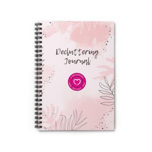 May include: A pink and white spiral bound journal with the text "Decluttering Journal" and a pink heart logo with the text "A Hoarders Heart".