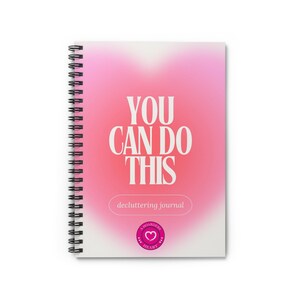 May include: A pink and white spiral bound journal with the text "YOU CAN DO THIS" in white letters. The journal has the text "decluttering journal" and a pink heart with the text "A Hoarder's Heart" on the front cover.