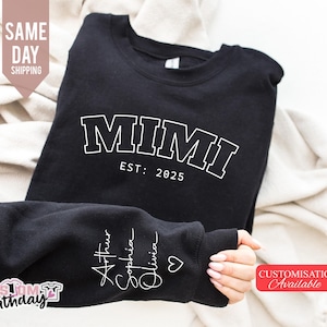 Könnte beinhalten: Schwarzer Pullover mit weißem Text, der "MIMI EST: 2025" lautet. Der Ärmel hat weißen Text, der "Arthur Sophia Olivia" mit einem Herzsymbol lautet.