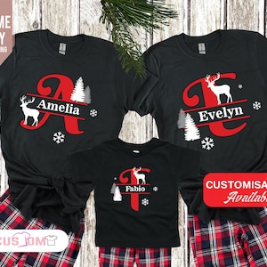 May include: Black Christmas shirts with red and white reindeer and tree designs. The shirts are personalized with the names Amelia, Evelyn, and Fabio. The shirts are paired with red and black plaid pants.