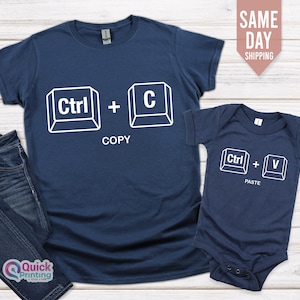 May include: A navy blue t-shirt with the text "Ctrl + C" and the word "COPY" underneath. A navy blue baby onesie with the text "Ctrl + V" and the word "PASTE" underneath.