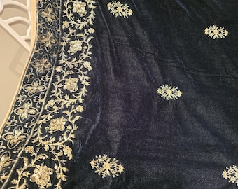 May include: A dark blue velvet shawl with intricate gold embroidery along the border and scattered across the surface. The gold embroidery features floral and leaf patterns, adding a touch of elegance to the textile.