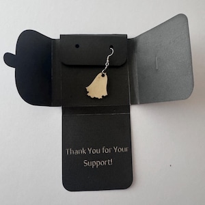 May include: A single ghost-shaped earring made of light-coloured wood hangs from a silver hook. The earring is displayed on a black card with the text "Thank You for Your Support!" The card is inside a black gift box.