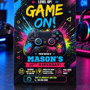 May include: A rectangular birthday invitation card featuring a black background with colorful paint splatters and a central game controller graphic. Text includes LEVEL UP! GAME ON!, MASON'S 10TH BIRTHDAY!, event details for June 21, 2026, at Power Play Arena, and RSVP information.