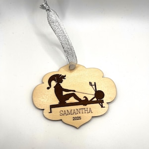 May include: Wooden ornament with a silhouette of a person rowing on a machine. The ornament is shaped like a cloud and has the name "SAMANTHA" and the year "2025" engraved on it. A silver ribbon is attached for hanging.