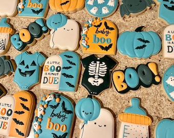 Könnte beinhalten: Eine Auswahl an Halloween-Keksen mit verschiedenen Designs. Enthält Geister-, Kürbis- und Baby-Kekse. Farben sind Orange, Türkis, Weiß und Schwarz. Einige Kekse tragen die Aufschrift "baby boo" und "a little boo is almost due".