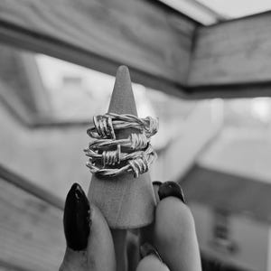 Könnte beinhalten: Ein silberner Ring mit einem Stacheldraht-Design. Der Ring wird auf einem kegelförmigen Ständer präsentiert.
