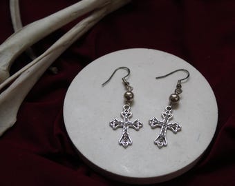 May include: A pair of silver cross earrings with a small silver bead on each earring. The earrings are on a white surface.