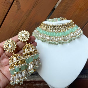 May include: A gold and green beaded necklace and earrings set. The necklace has multiple layers of beads, including pearls, green glass beads, and gold accents. The earrings are dangle earrings with a similar design to the necklace.