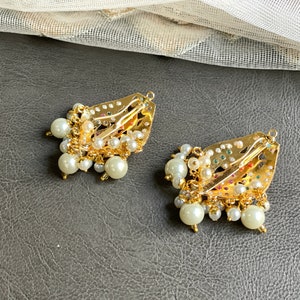 May include: Two gold hair clips with intricate designs and pearl embellishments. The clips are decorated with colorful stones and have a dangling pearl fringe.