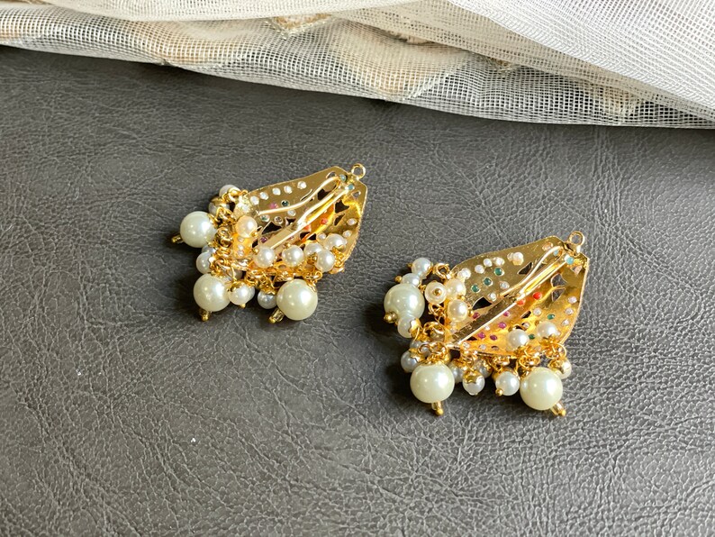May include: Two gold hair clips with intricate designs and pearl embellishments. The clips are decorated with colorful stones and have a dangling pearl fringe.