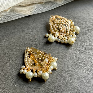 May include: Two gold-tone hair clips with pearl embellishments. Each clip features a delicate, intricate design and is adorned with a cluster of white pearls.