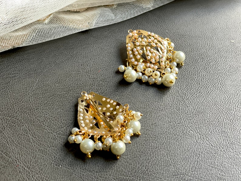 May include: Two gold-tone hair clips with pearl embellishments. Each clip features a delicate, intricate design and is adorned with a cluster of white pearls.