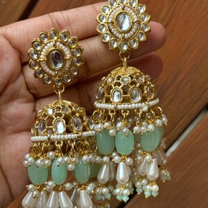 May include: Gold earrings with a round, ornate design and a dangling section of green and white beads.
