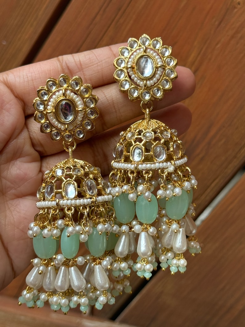 May include: Gold earrings with a round, ornate design and a dangling section of green and white beads.