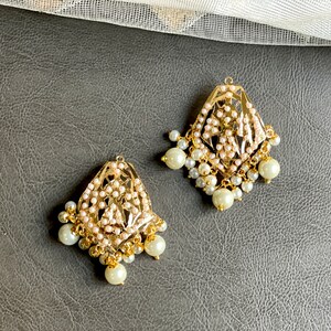 May include: A pair of gold earrings with intricate designs and white pearl accents.