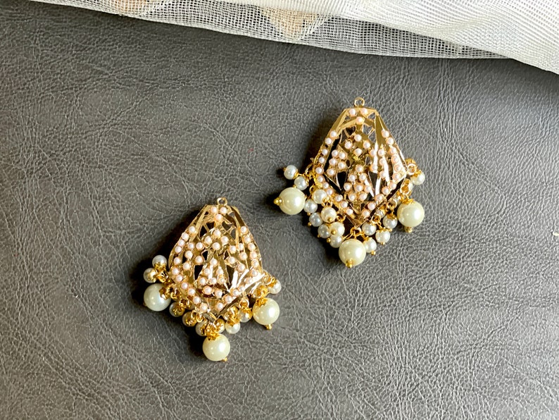 May include: A pair of gold earrings with intricate designs and white pearl accents.