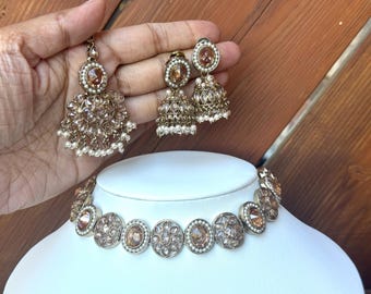 Pode incluir: Um colar choker de ouro e pérolas com uma pedra grande, redonda, de cor castanho claro no centro de cada pendente. O colar é combinado com brincos combinando com um design semelhante.