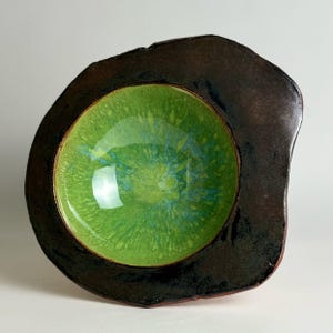 May include: A ceramic bowl with an irregular, organic shape featuring a glossy, vibrant lime green interior with subtle blue speckles. The wide, flat rim has a dark, textured, matte brown finish that contrasts with the bright, smooth center.
