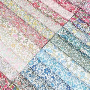 Op de afbeelding: Een verzameling gevouwen stroken stof met een verscheidenheid aan ingewikkelde bloemmotieven in diverse kleurenpaletten, waaronder tinten roze, geel, blauw, groen en wit. De stoffen zijn in parallelle rijen gerangschikt en tonen dichte botanische prints.