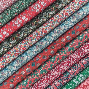 Könnte beinhalten: Eine Sammlung von Stoffballen, die diagonal angeordnet sind und verschiedene Blumen- und Pflanzenmuster in Rot-, Grün-, Blau- und Weißtönen aufweisen. Die Designs zeigen detaillierte Illustrationen von kleinen Vögeln, Beeren und Blüten.