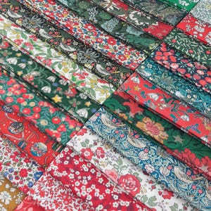 Pode incluir: Uma coleção de tiras de tecido dobradas com vários padrões botânicos e aviários complexos. Os designs incluem motivos florais, bagas, folhas e pequenos pássaros em vermelho, verde, branco e azul, dispostos em composições densas e repetitivas.