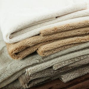 May include: A stack of plush fabric in various shades of brown, beige, and white. The fabric is soft and fluffy, with a luxurious feel.