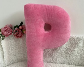 Könnte beinhalten: Ein rosa Plüschkissen in Form des Buchstabens P. Das Kissen ist aus weichem, samtigem Stoff gefertigt und perfekt, um jedem Raum eine persönliche Note zu verleihen.
