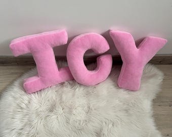 May include: Pink plush letters spelling out the word "ICY" on a white fluffy rug.