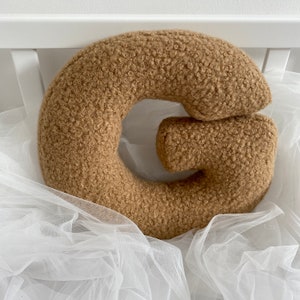 Puede incluir: Una almohada de peluche marrón en forma de letra G. La almohada está hecha de un material suave y esponjoso y tiene la forma de la letra G. Es una gran adición a una guardería o habitación infantil.
