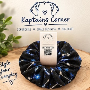 May include: A black fabric scrunchie featuring a blue and white star constellation pattern. A white paper tag is inserted through the center, displaying the text Kaptains Corner, a QR code, and the phrase CHECK OUT OUR ETSY.