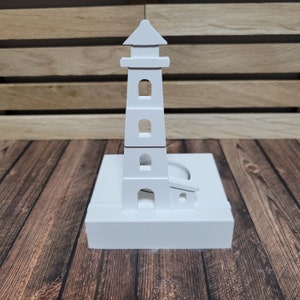 Könnte beinhalten: Weißer Holz-Leuchtturm-Kerzenhalter mit quadratischer Basis und drei Fenstern. Der Kerzenhalter ist für ein Teelicht konzipiert.