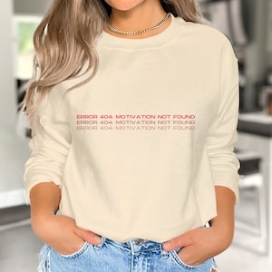 May include: A cream-coloured long-sleeved sweatshirt with the text "ERROR 404: MOTIVATION NOT FOUND" repeated three times in pink.