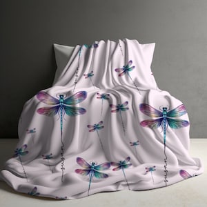 May include: White throw blanket with a repeating pattern of colorful dragonflies and the word "whisper" written vertically on the fabric.